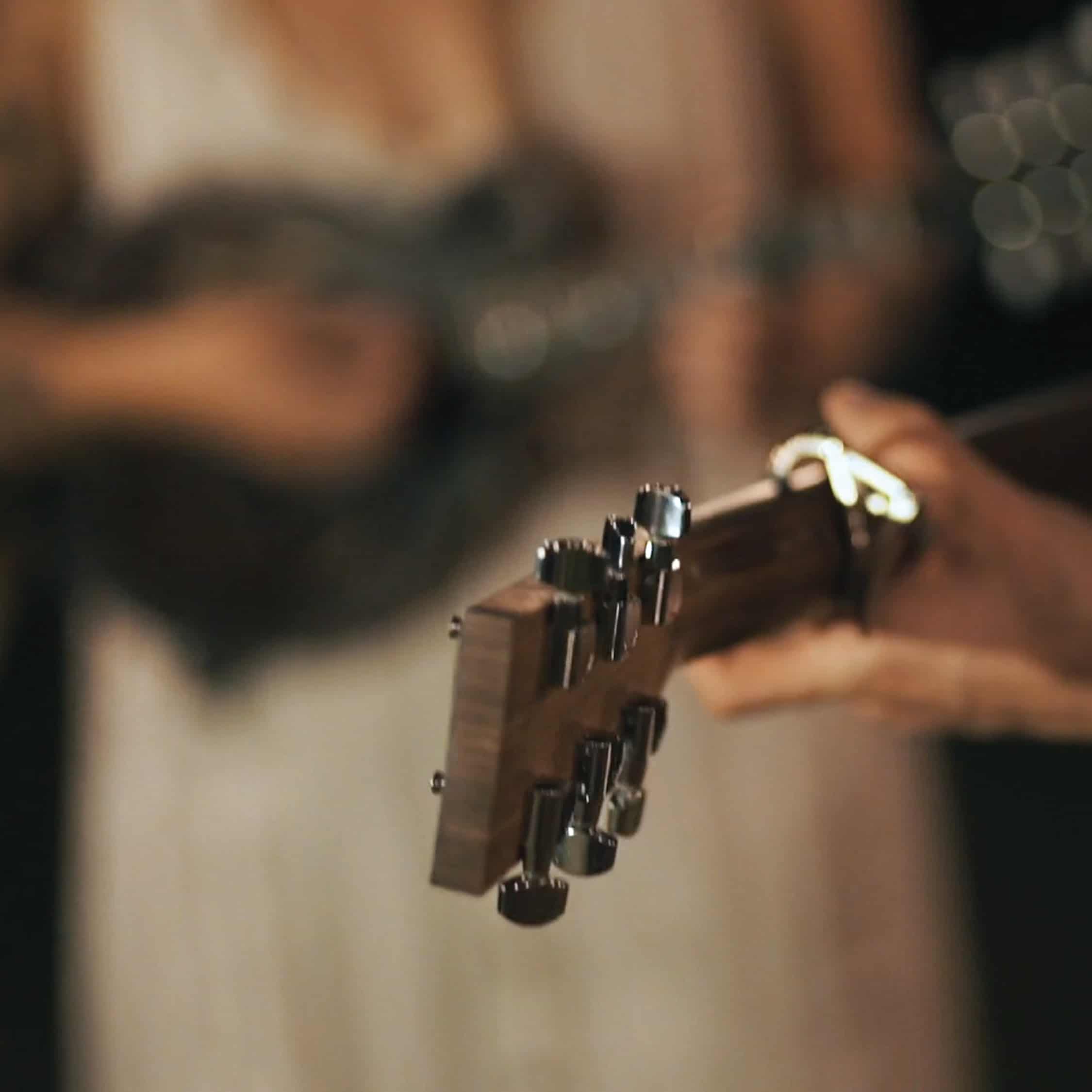 A hand holds up a guitar. Someone out of focus strums another guitar.