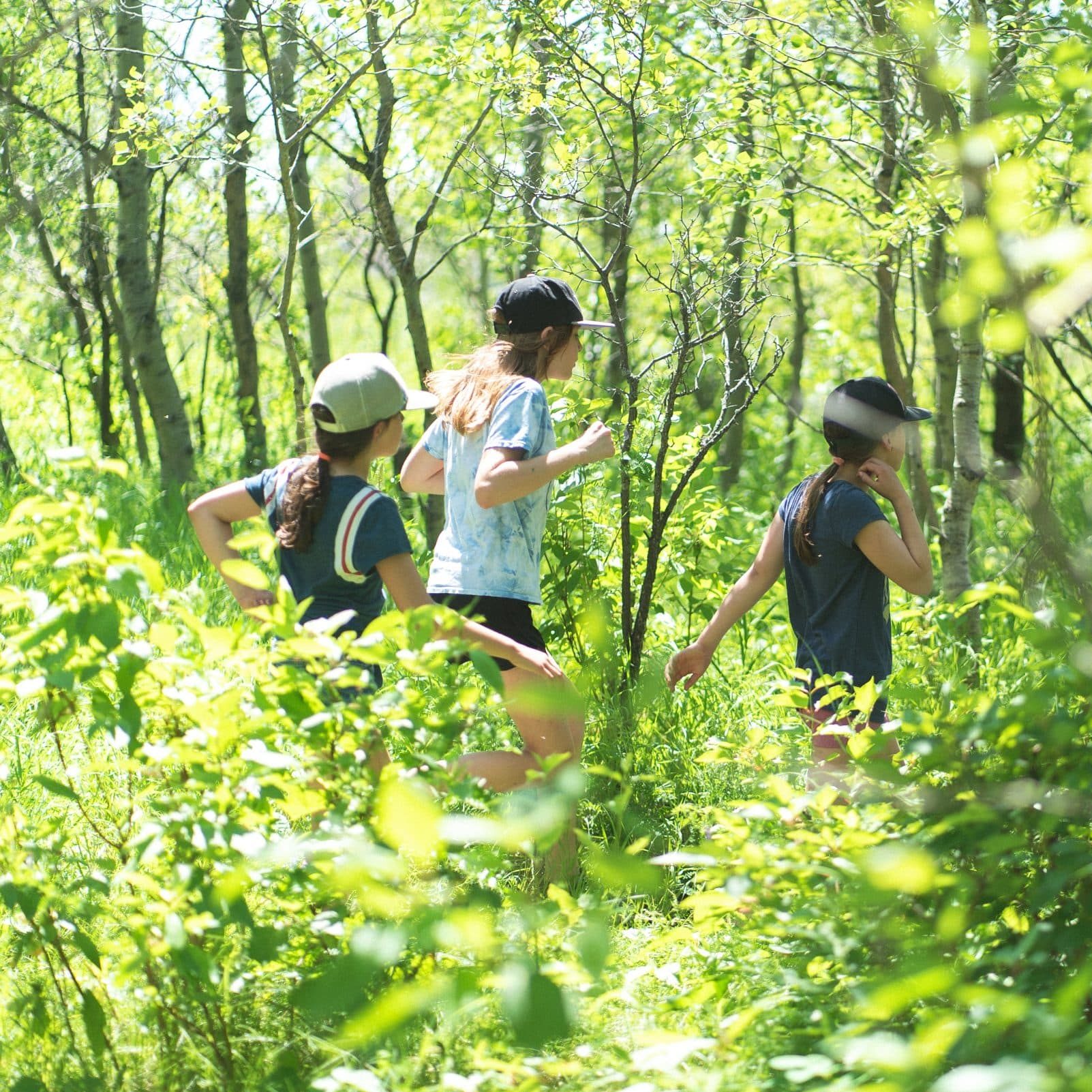 Group of children running through forest as seen through trees.