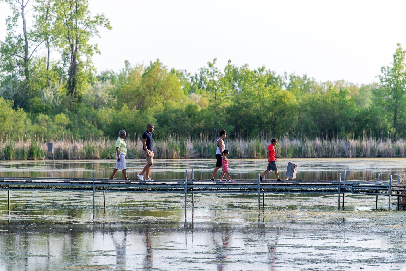 Three adults and two small children walk along the boardwalk in summer