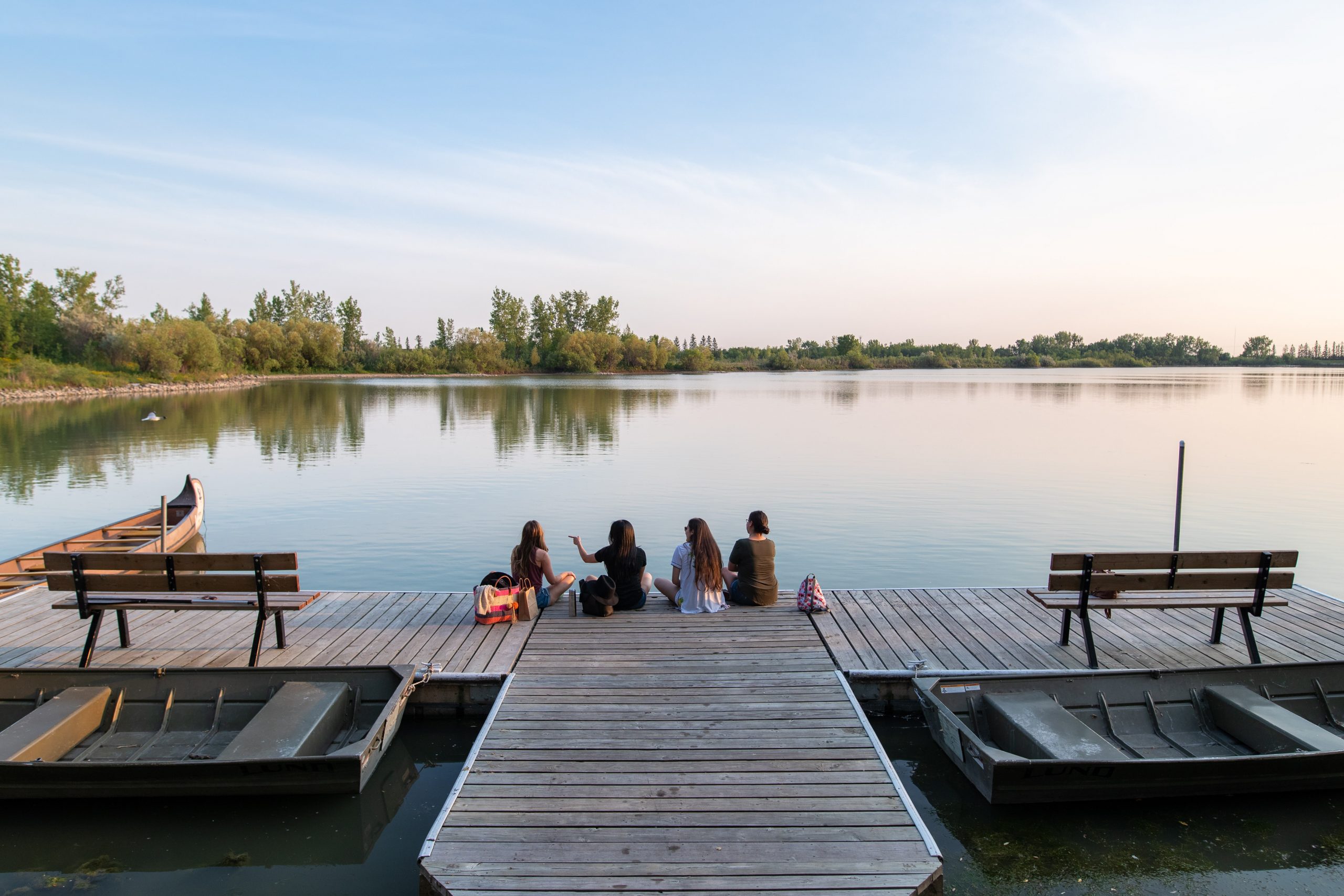 Four adults sit on the dock looking at the lake.