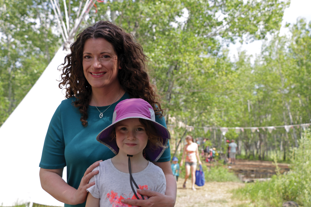 Dana stands behind Tessa with the forest behind them