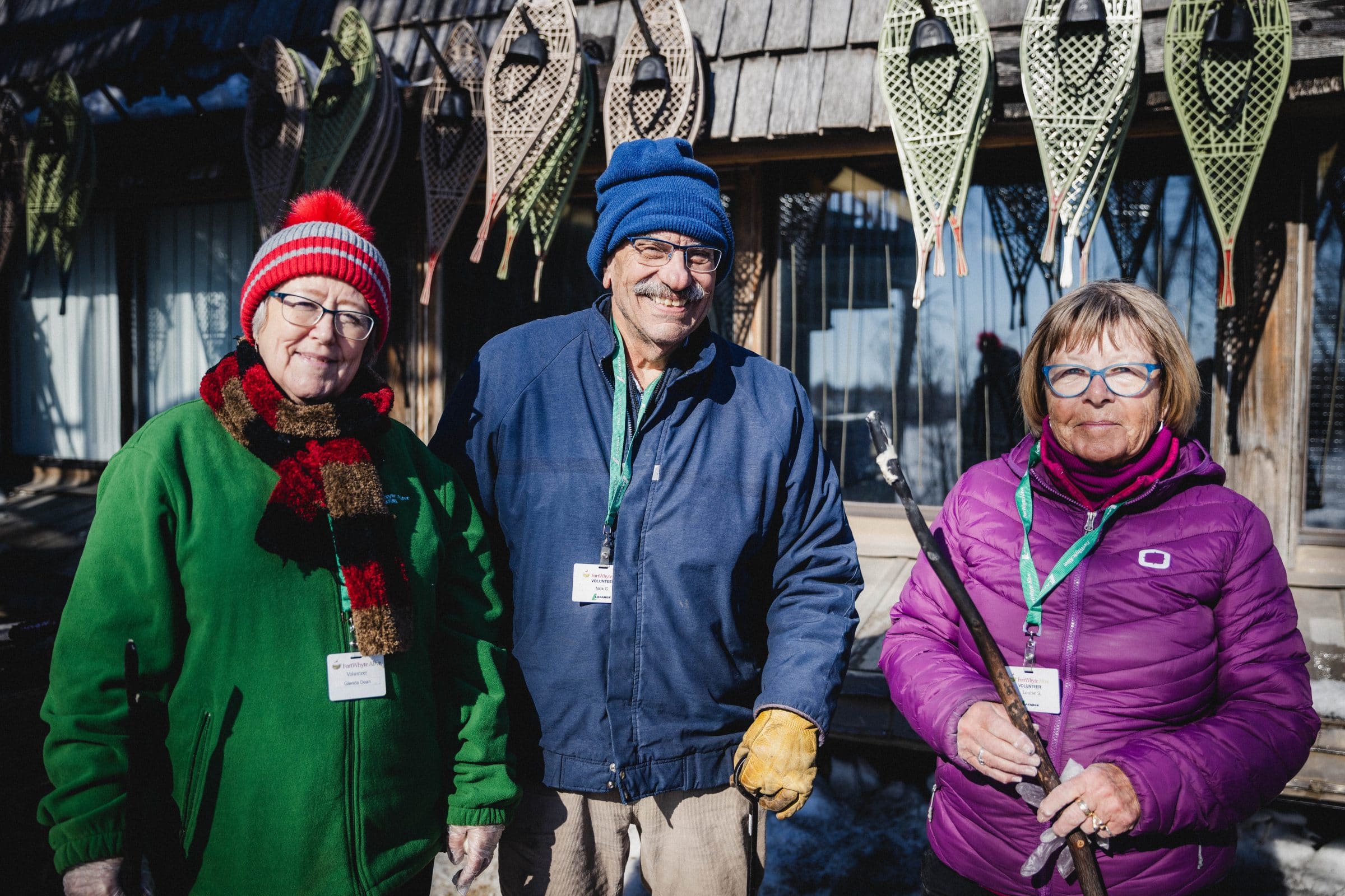 Three adults smile at the camera. They wear lanyards that indicate they are volunteers.