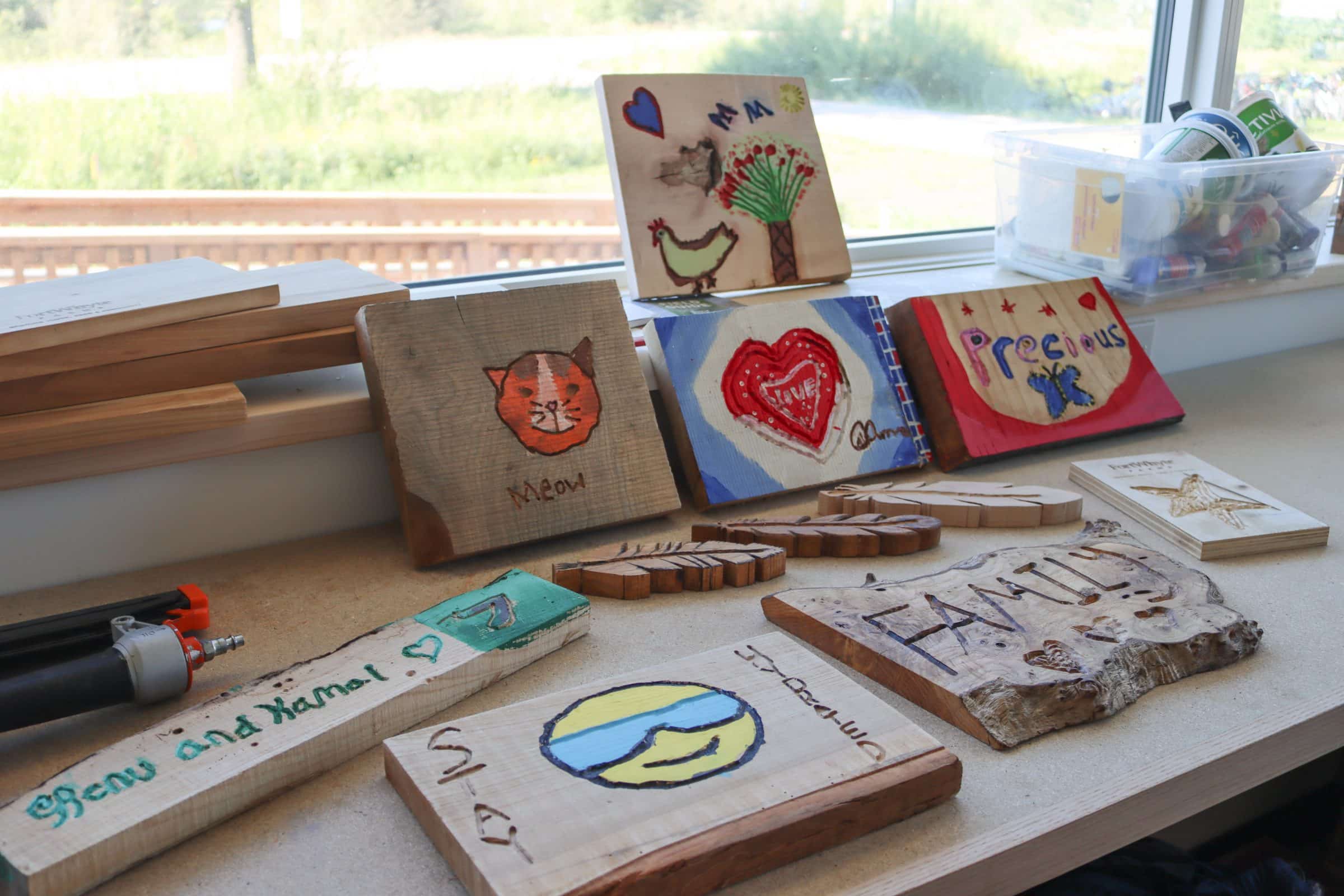An assortment of small wooden boards with designs, names, and colours on them made by farm youth.