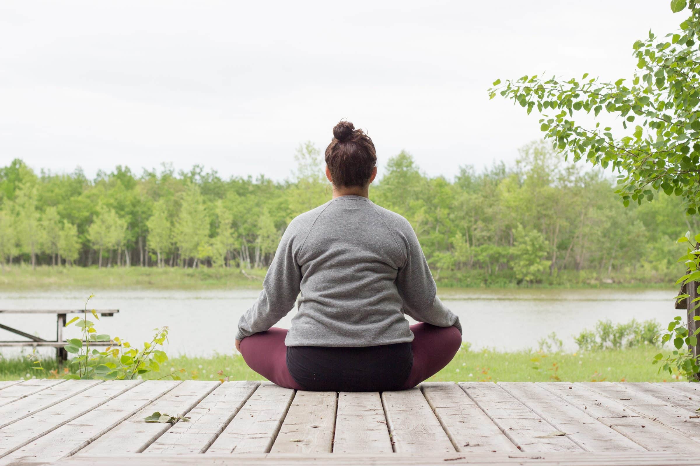 Person sitting on deck of cabin in crossed legged yoga pose.