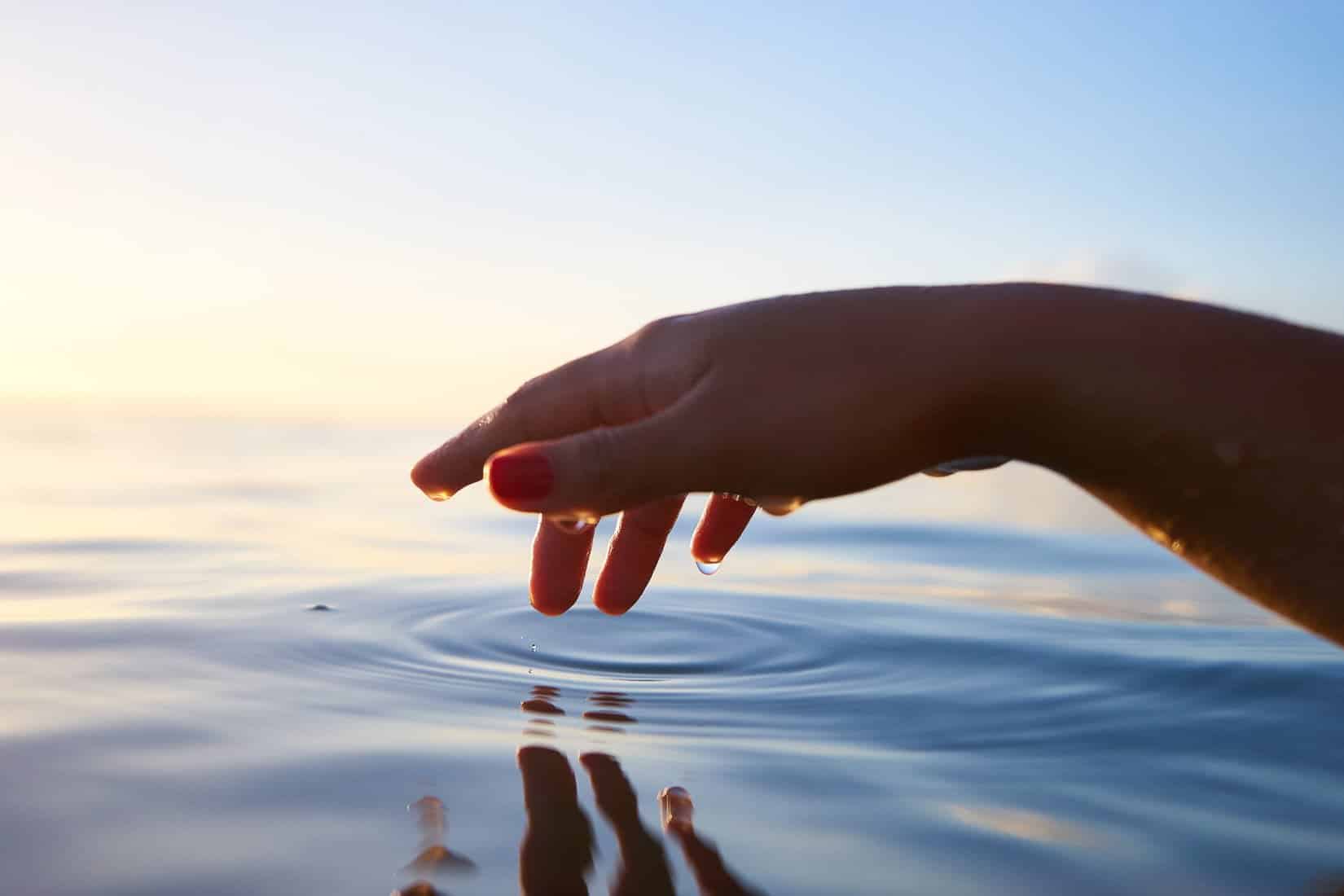 Hand gently touching waters surface.