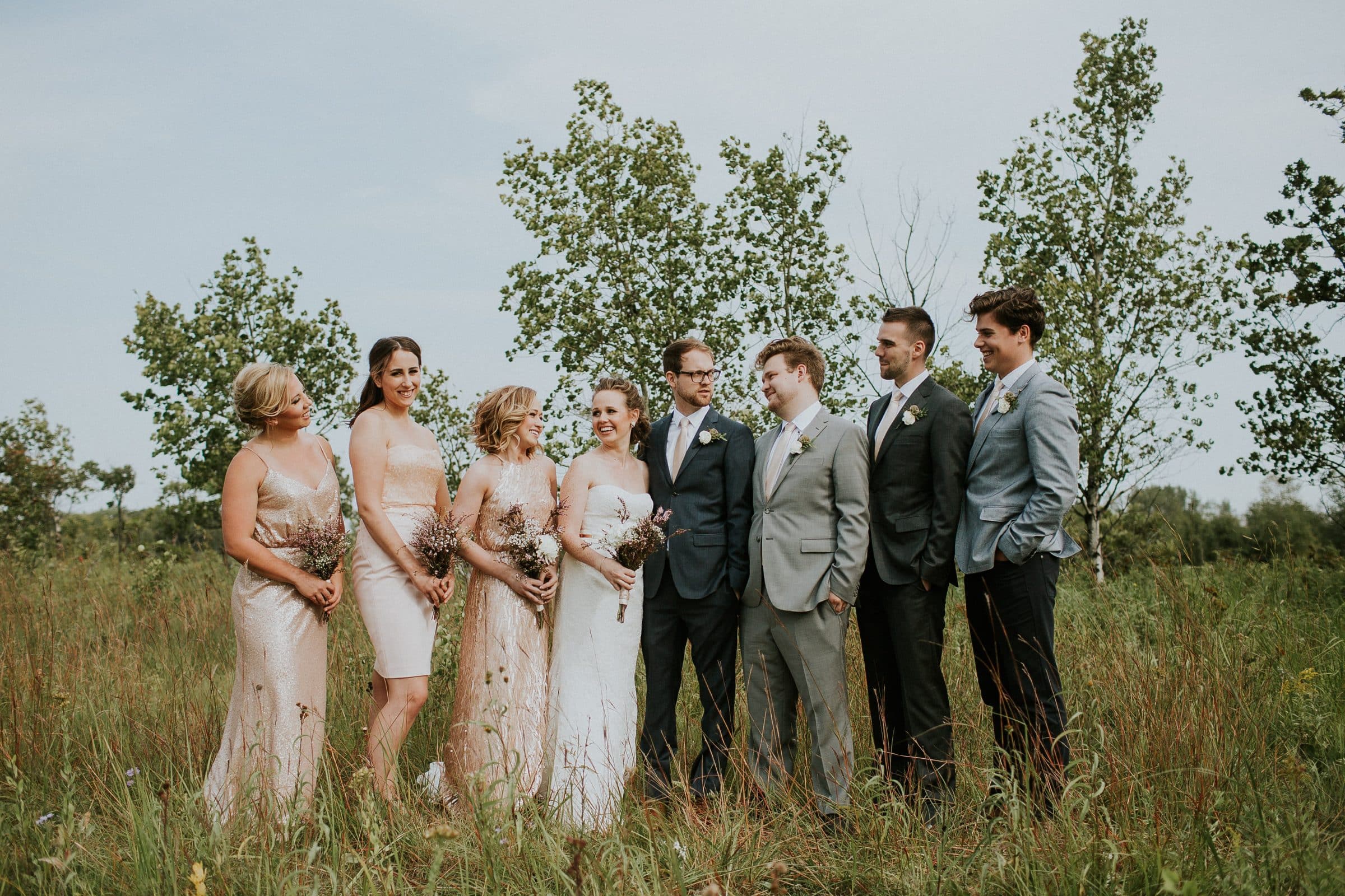Wedding party stands in grassy field.