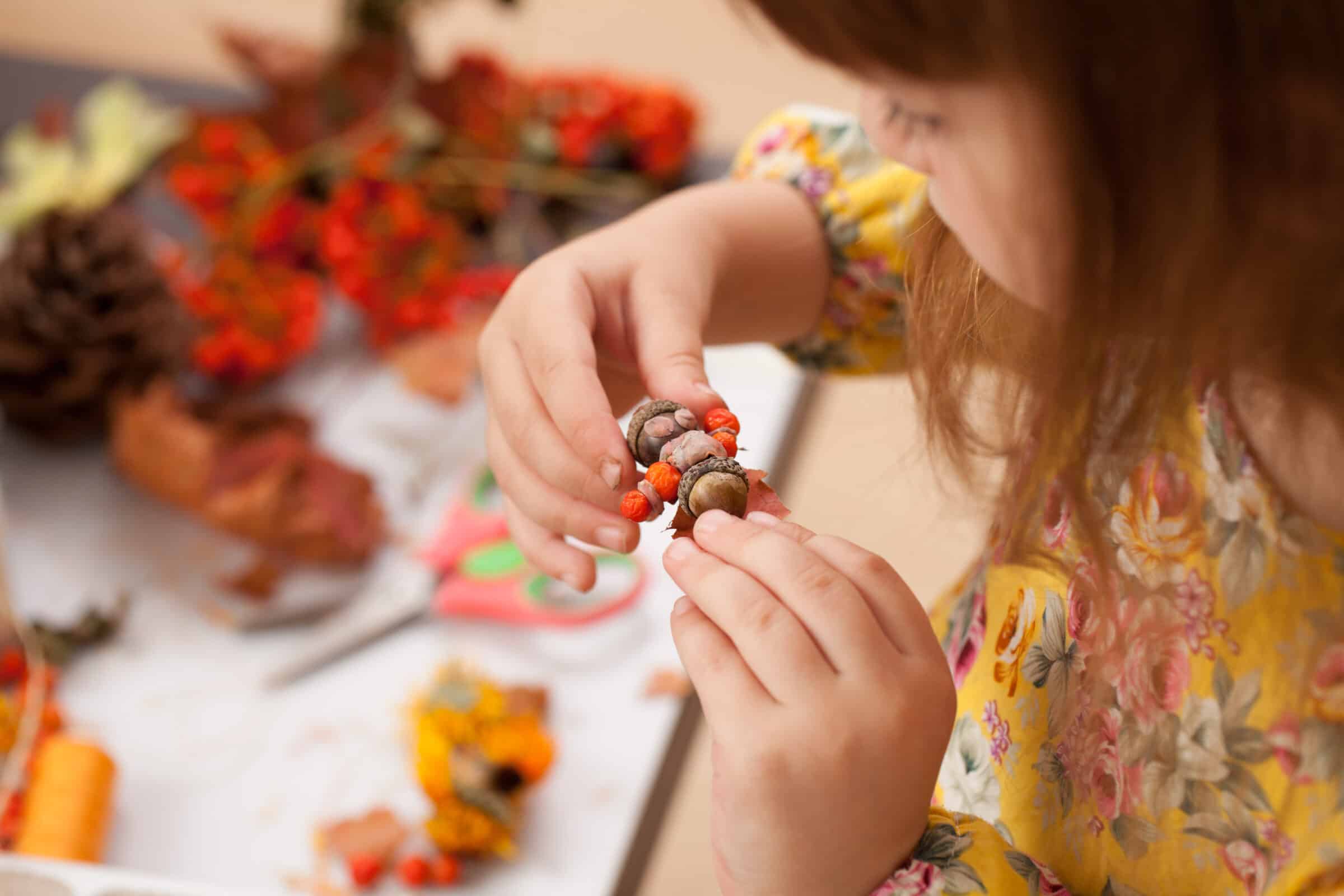 Child holding craft made of acorns over table of other craft materials.