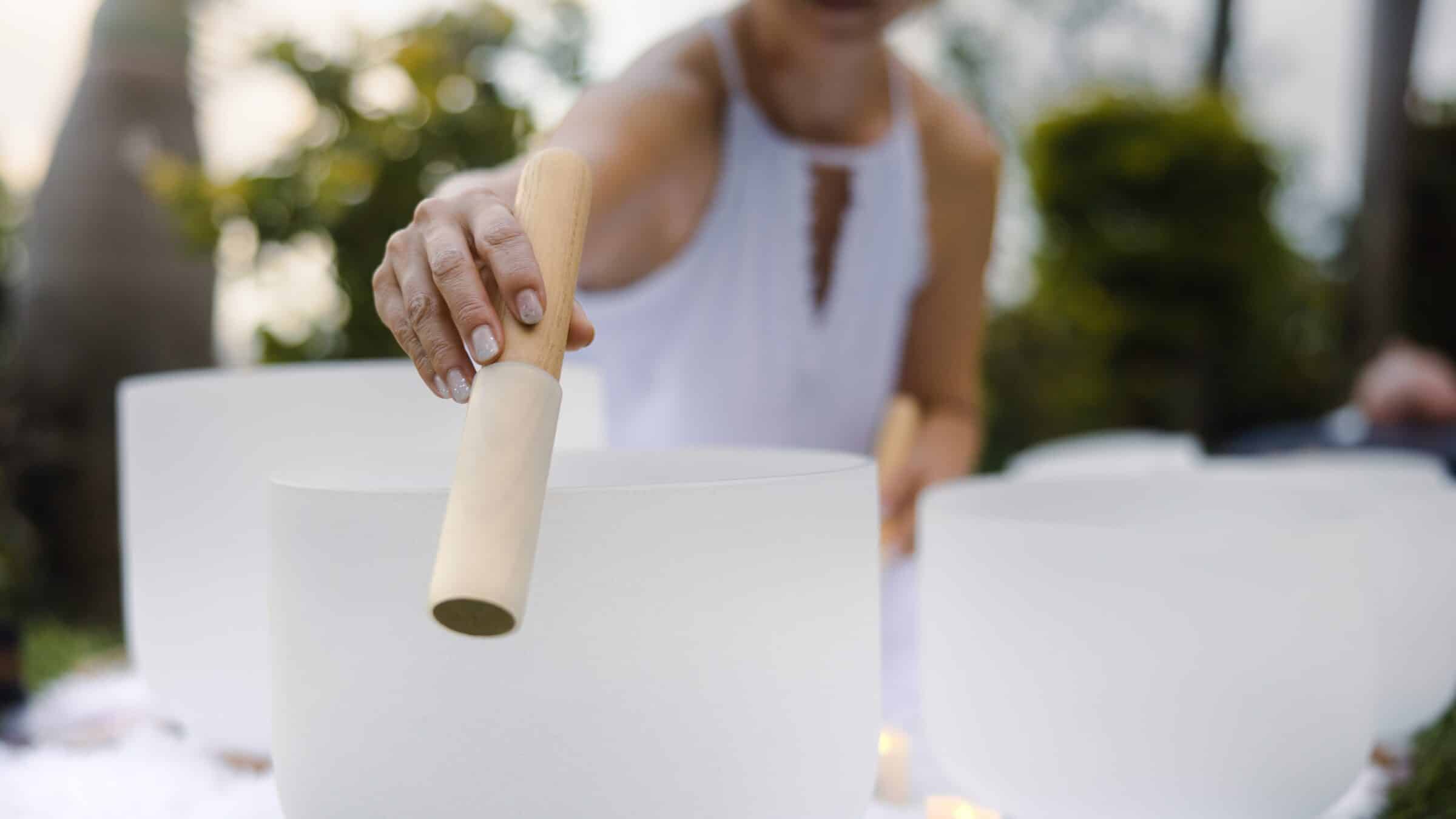 person holding stick to edge of crystal singing bowl