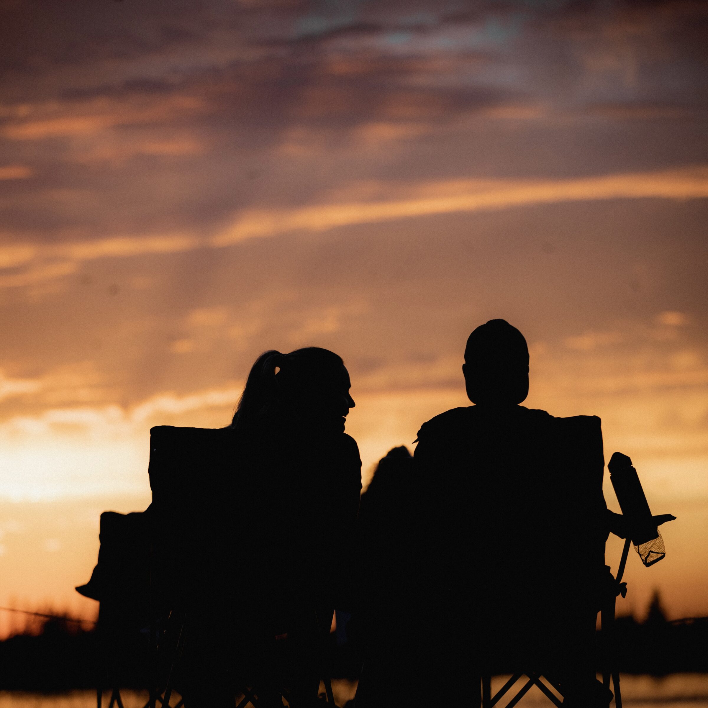 Two people sit in lawn chairs facing sunset.